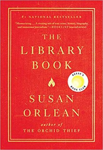 A simple cover. The entire book is red. All of the font is straw colored/ harvest gold and contained within a simple double bordered space slightly smaller than the face of the book. The main text is The Library Book, a small flame icon, and Susan Orlean. Above this in smaller font is a short review. Below the main text, in smaller font is the title of another book by the author - The Orchid Thief. 